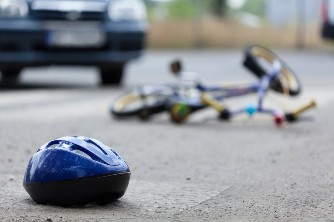 Childs bike helmet and bike on road, car in background