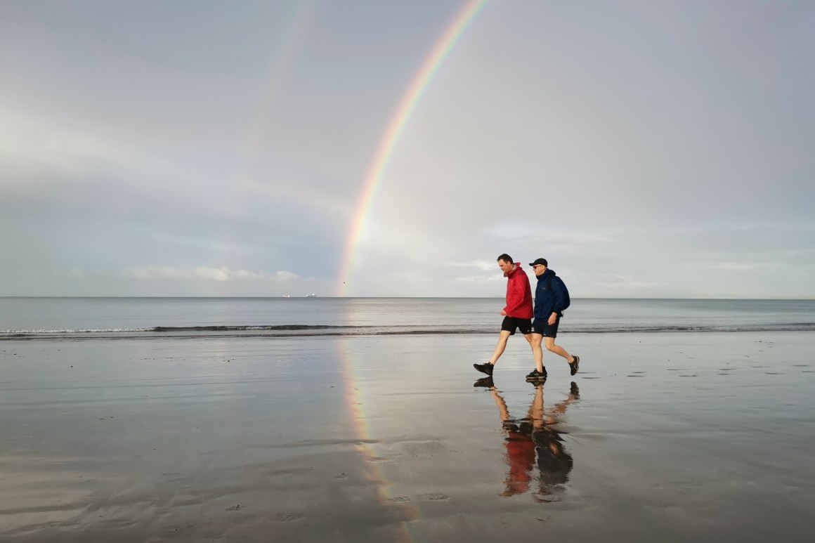 men walking on wet sand with rainbow